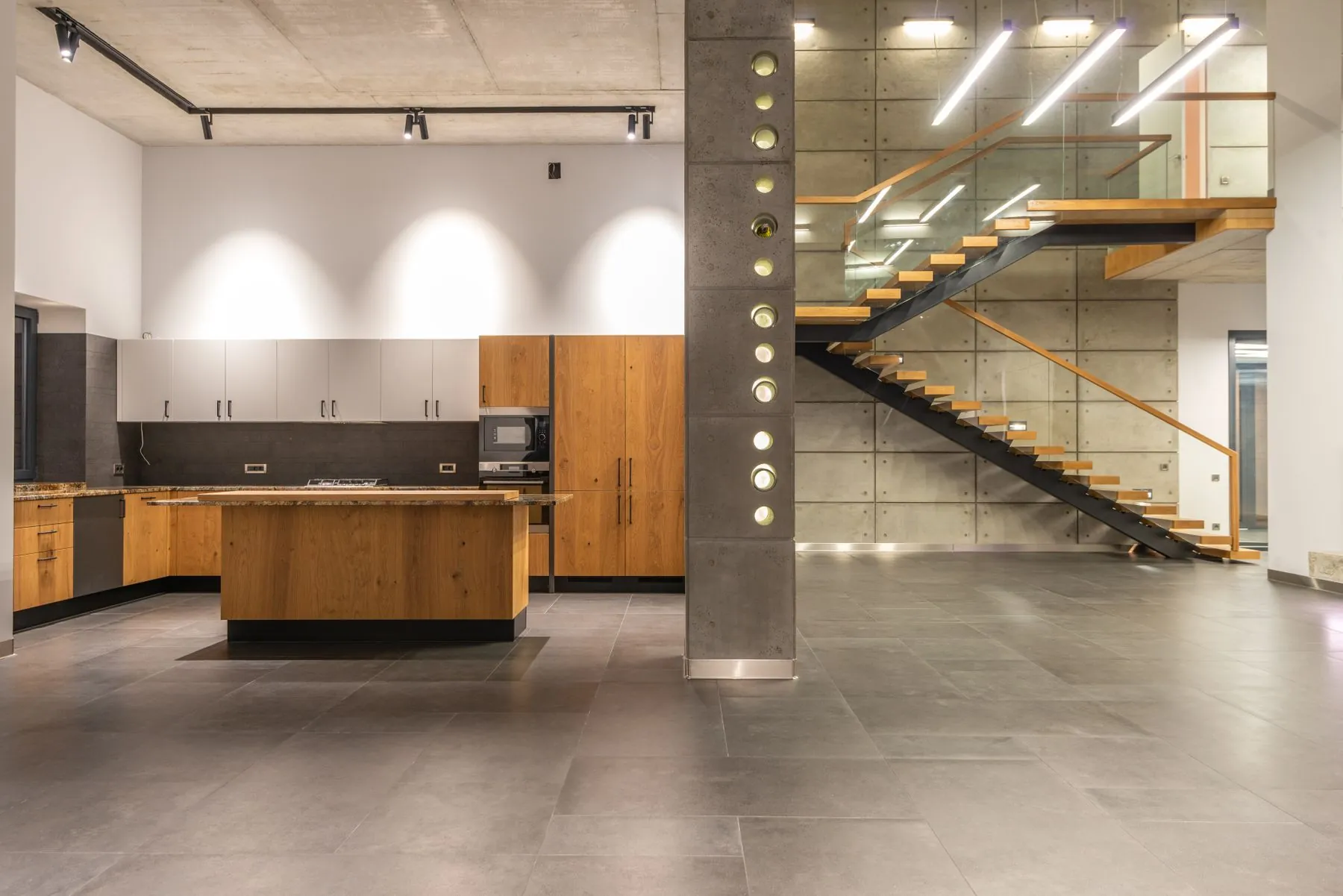 An open kitchen with a floating staircase and wood cabinets